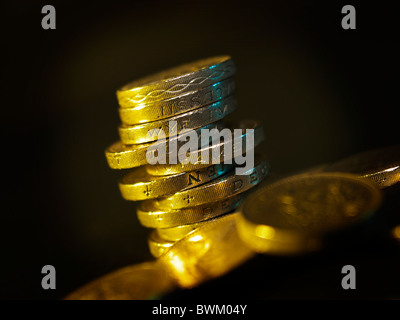 Una pila di British pound monete con illuminazione soffusa si alzò in piedi tra le altre monete cancelletto Foto Stock