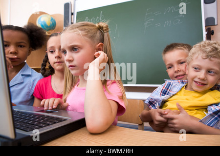 Foto di smart schoolgirl guardando il portatile con i suoi compagni sullo sfondo Foto Stock