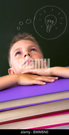 La faccia di un diligente scolaro guardando verso l'alto con la sua testa sulla pila di libri su sfondo nero Foto Stock