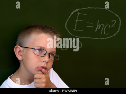 Foto di pensieroso lad dalla lavagna toccando il suo mento mentre il pensiero di difficile formula Foto Stock