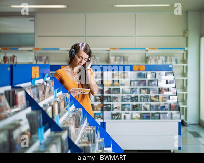 La donna caucasica con le cuffie, scegliere cd nel negozio di musica. Sagoma orizzontale, vista frontale, vita, spazio di copia Foto Stock