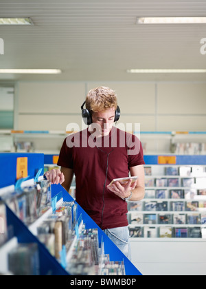 Uomo caucasico con le cuffie, scegliere cd nel negozio di musica. Forma verticale, vista frontale, vita, spazio di copia Foto Stock