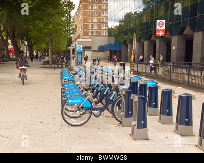Una linea di nuovo noleggio biciclette situato in una trafficata strada di Londra con la stazione della metropolitana di Londra segno e alto edificio uffici e appartamenti. Foto Stock
