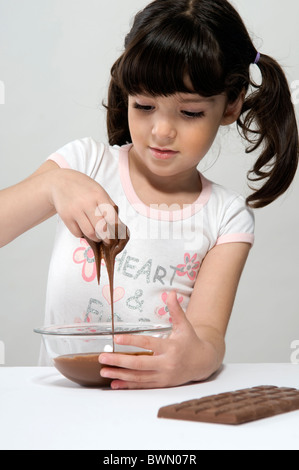 Ragazza di mettere la sua mano in una pentola piena di cioccolato fuso e una barra di cioccolato sul tavolo Foto Stock