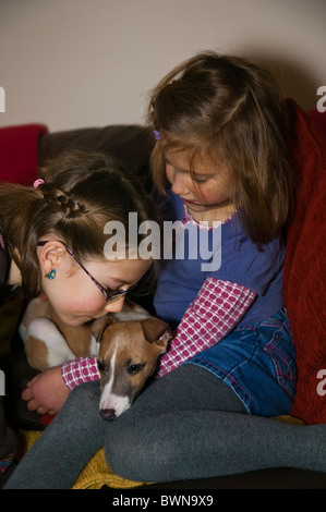 Due piccole bambine età da 5 a 7 delle coccole un cucciolo sul divano Foto Stock