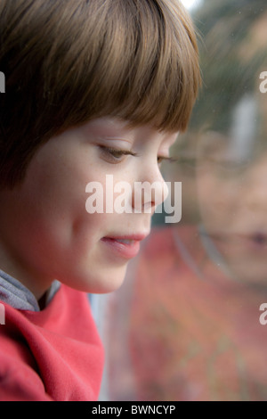 Ragazzo che guarda verso il basso accanto a una finestra Foto Stock