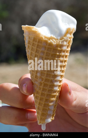 Mano che tiene una fusione di gelato in un cono con un gocciolamento Foto Stock