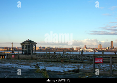 Capanna abbandonati sul molo sul fiume Mersey con traghetti passeggeri ormeggiata sulla riva opposta del fiume. Foto Stock