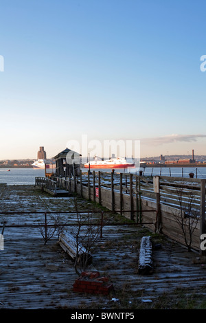 Capanna abbandonati sul molo sul fiume Mersey con traghetti passeggeri ormeggiata sulla riva opposta del fiume. Foto Stock