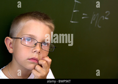 Foto di pensieroso lad dalla lavagna toccando il suo mento mentre il pensiero di difficile formula Foto Stock