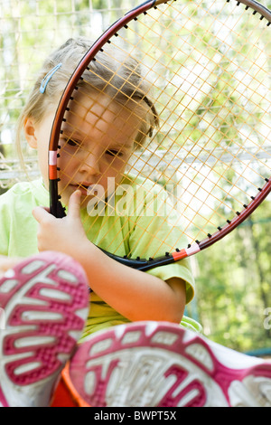 Triste bambino con la racchetta da tennis guardando attraverso la sua rete all'aperto durante le vacanze Foto Stock