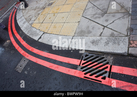 Matrimoniale Rossa linee curve intorno al marciapiede di una strada di Londra. Foto Stock