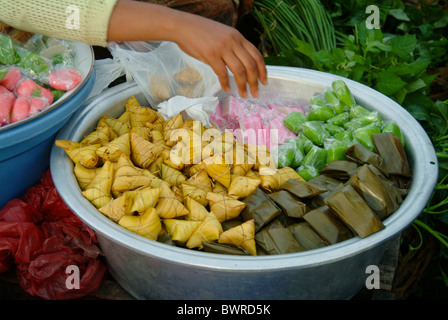 In un tradizionale mercato all'aperto in Ubud, Bali, un venditore sacchi alcuni dessert Balinese considera perfettamente avvolto in prodotti naturali. Foto Stock