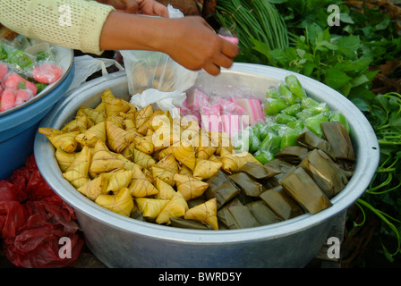 In un tradizionale mercato all'aperto in Ubud, Bali, un venditore sacchi alcuni dessert Balinese considera perfettamente avvolto in prodotti naturali. Foto Stock