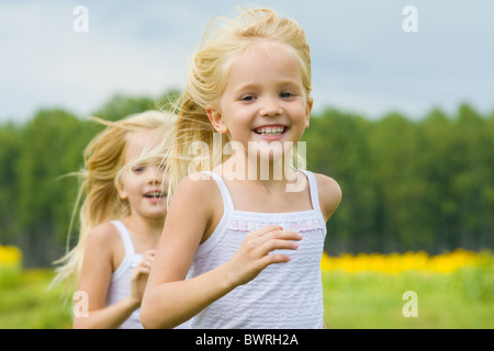 Ritratto di ragazza carina in esecuzione e sorridente in telecamera con la sua sorella gemella sullo sfondo Foto Stock