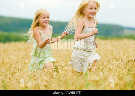 Ritratto di felice Ragazza che corre verso il basso campo di grano con la sua sorella gemella dietro Foto Stock