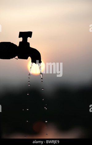 Silhouette di un tubo di supporto tocca all'alba con il gocciolamento di acqua Foto Stock
