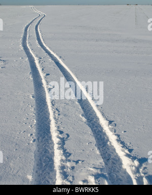 Cingoli gommati effettuati da un veicolo agricolo attraverso una coperta di neve campo. Foto Stock