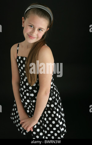 Carino dieci anno vecchia ragazza indossando un archetto e una polka dot dress. Foto Stock