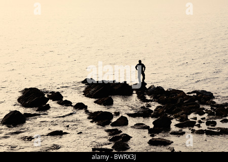 Lone figura in piedi sulle rocce guardando il mare Foto Stock