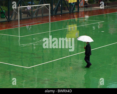 Un uomo con un ombrello bianco che attraversa un campo di calcio sotto la pioggia in hong kong Foto Stock