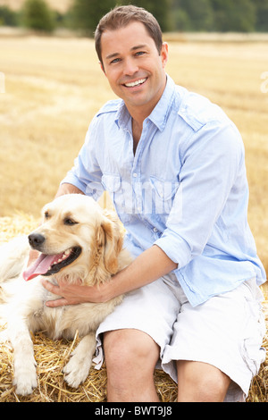 Uomo seduto con cane in balle di paglia nel campo di raccolto Foto Stock