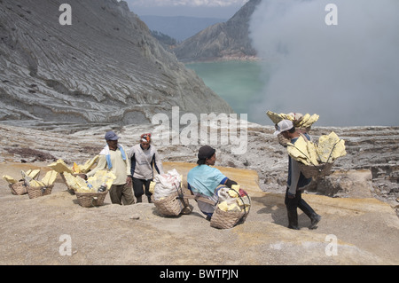 Uomo locale con blocchi di zolfo in cestelli, in appoggio sul percorso intorno al cratere vulcanico, vicino turchese-verde acido colorato Foto Stock