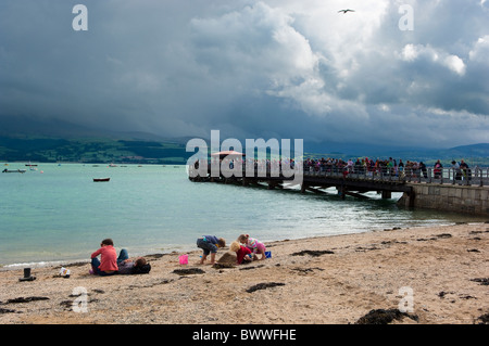 La spiaggia a Beaumaris, Isola di Anglesey, mostrando un pontile e gruppo familiare sulla sabbia. Persone attività di pesca del granchio sul pontile. Foto Stock