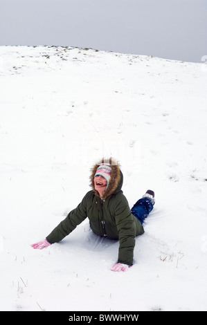 Giovane ragazza ridere come lei scorre giù per una coperta di neve pendenza Foto Stock