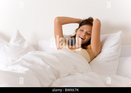 Camera da letto - donna svegliarsi e stretching nel letto bianco Foto Stock