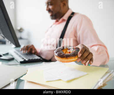 African American imprenditore ciambella di mangiare alla scrivania Foto Stock