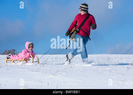 Donna tirando neonato ragazza sulla slitta di legno nel paesaggio invernale, Dobel, Foresta Nera, Gerrmany Foto Stock