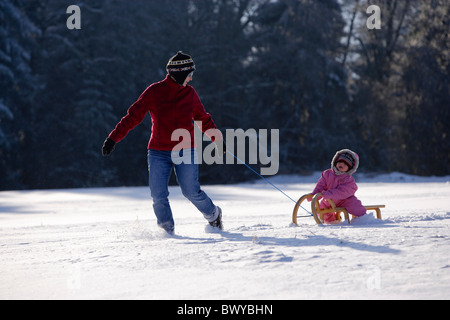 Donna tirando neonato ragazza sulla slitta di legno nel paesaggio invernale, Dobel, Foresta Nera, Germania Foto Stock