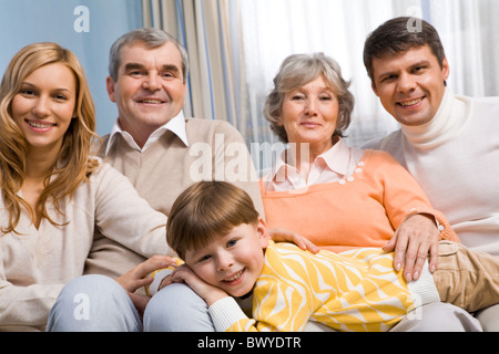 Ritratto di ragazzo carino che giace sulle ginocchia di genitori e nonni e guardando la fotocamera Foto Stock