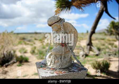 Pregando angelo alato scolpito in pietra decorata con collane e monete, situato al lato della strada vicino alla cima, California, USA. Foto Stock