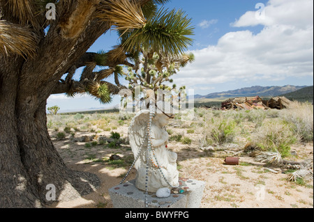 Pregando angelo alato scolpito in pietra decorata con collane e monete, situato a lato strada vicino a Joshua Tree. Foto Stock