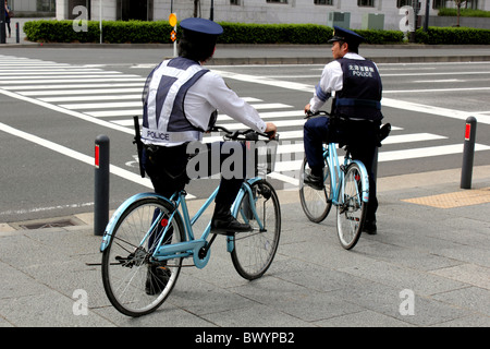 Due poliziotti giapponesi sulle biciclette attendere alla croce di attraversamento pedonale Yokohama Giappone Foto Stock
