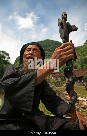 Anziani Yao Miao sacerdote in costume tradizionale con un legno intagliato scettro Longlin, Baise, provincia di Guangxi, Cina Foto Stock