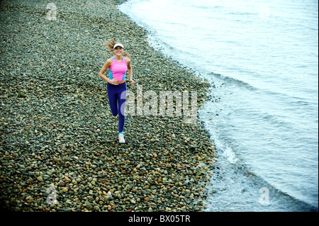 La donna caucasica in esecuzione sulla spiaggia ghiaiosa Foto Stock