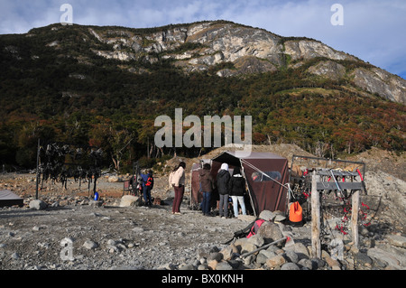 Ice-trekking turisti in un rampone-raccordo tenda stazione sulla morena al di sotto di una foresta di lenga hillside, il Ghiacciaio Perito Moreno, Ande Foto Stock