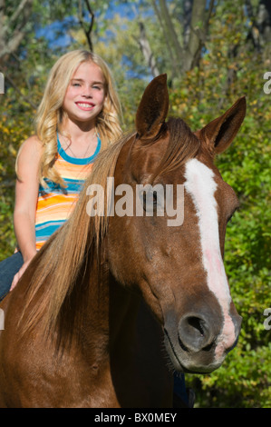 Bella ragazza bionda sul cavallo di castagno godendo di un giro, equitazione close up ritratto. Foto Stock