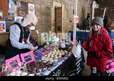 Durham Xmas mercato entro il chiostro della Cattedrale di Durham. Una ragazza acquista prodotti dolciari da questo stallo. Foto Stock