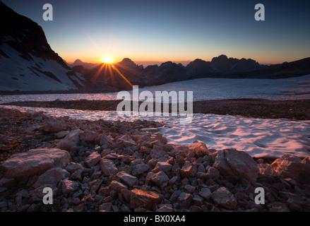 The sun dips down below the mountains in the Julian Alps in Slovenia. Image was taken 300 metres below the summit of Triglav. Foto Stock