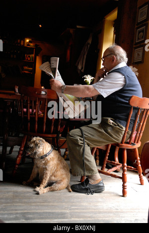 Uomo seduto in un pub con il suo cane quotidiano di lettura Foto Stock