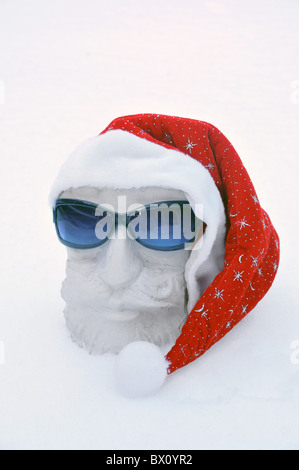 Un'argilla santa claus si assomigliano testa indossando sfumature, / gli occhiali da sole e cappello e seduta nella neve. Foto Stock