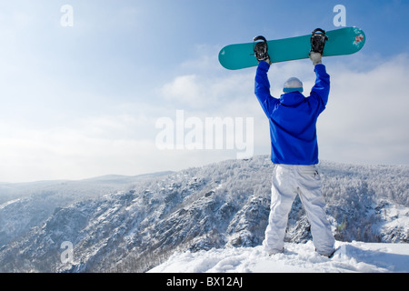 Vista posteriore di uno sportivo con lo snowboard in piedi sulla cima del monte Foto Stock