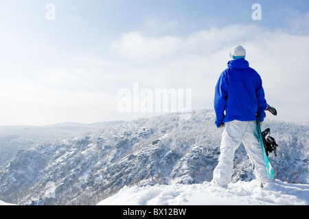 Vista posteriore di uno sportivo con lo snowboard in piedi sulla cima del monte Foto Stock