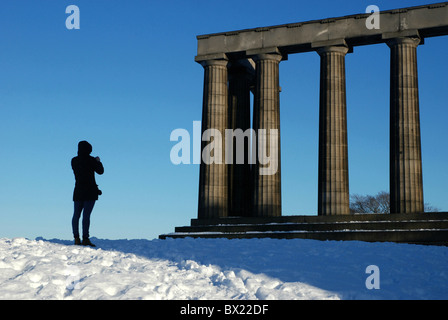 Un turista scattare fotografie del Monumento Nazionale su Calton Hill, Edimburgo, Scozia, Regno Unito dopo una caduta di neve. Foto Stock