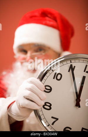 Foto di un orologio che mostra cinque minuti a mezzanotte con Santa sullo sfondo Foto Stock