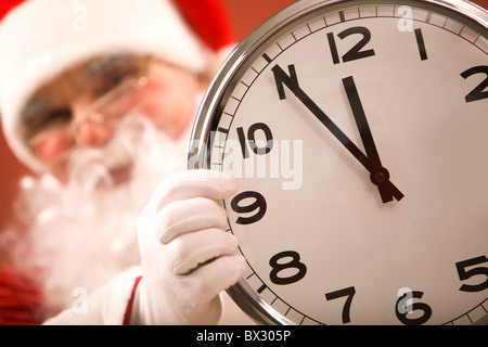 Foto di un orologio che mostra cinque minuti a mezzanotte con Santa sullo sfondo Foto Stock